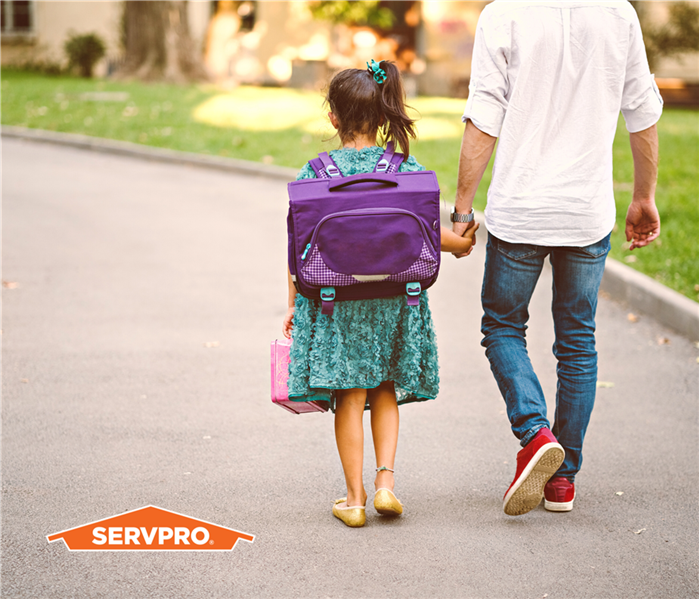 little girl and father holding hands, we see them from behind, she has a backpack going to school, SERVPRO logo in left corne