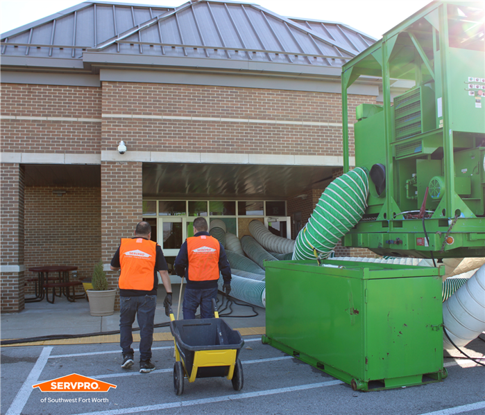 Two SERVPRO of Southwest Fort Worth employees in orange vests walking into a school next to a big, green desiccant dehumidifi